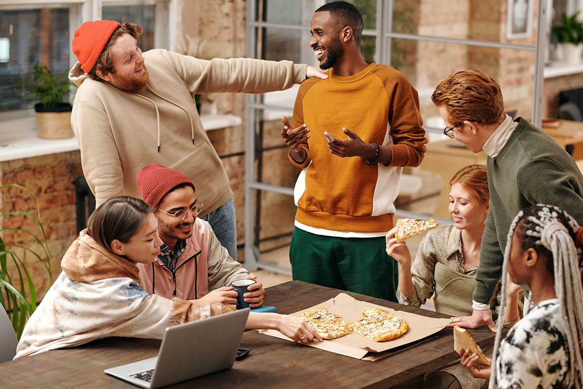 7 jeunes personnes discutent autour d'un ordinateur et une pizza