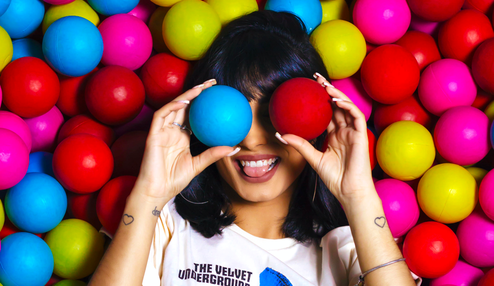Une femme est allongée au milieu de plusieurs balles colorées, elle en tient deux devant ses yeux et sourit en tirant la langue. C'est la photo principale de cet article rédigé par Eventdrivee
