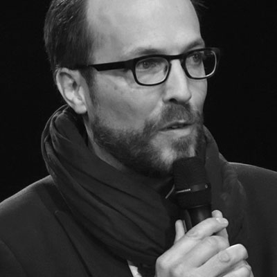 Un homme vêtu d'un foulard et de lunettes prend la parole au micro