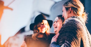 Trois amies rient ensemble dans une ambiance chaleureuse et ensoleillée. L'une d'elles porte un chapeau, et toutes partagent un moment de complicité en extérieur. - Article de blog Eventdrive