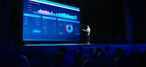 Une femme présente un graphique détaillé sur scène à un large auditoire attentif, dans le cadre d'un lancement de produit. - Article de blog Eventdrive