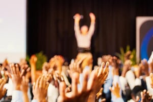 Un intervenant lève les bras face à son audience, qui lui répond en levant également les bras, créant une atmosphère d'engagement collectif. - Article de blog Eventdrive