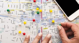 Carte de Montréal avec des punaises colorées marquant différents lieux, une main en train de placer une punaise verte, un smartphone posé en haut à droite. - Article de blog Eventdrive