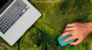 Main tenant une souris d’ordinateur sur un paysage verdoyant, à côté d’un ordinateur portable. - Article de blog Eventdrive