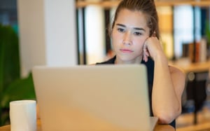 Une collaboratrice à l'air préoccupé devant son ordinateur portable, coude posé sur le bureau. - Article de blog Eventdrive