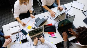 Une équipe travaille ensemble autour d’une table. Ils analysent des documents et des données sur plusieurs ordinateurs portables. - Article de blog Eventdrive