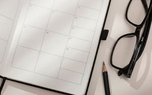 Agenda ouvert sur une page calendrier vierge, posé à côté d'un crayon et d'une paire de lunettes. - Article de blog Eventdrive