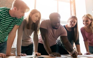 Groupe de six collaborateurs penchés autour d'une table, travaillant ensemble sur des documents lors d'un atelier de team building en entreprise - Article de blog Eventdrive