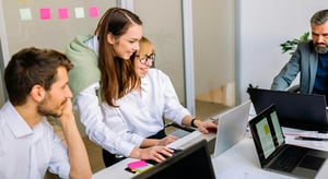 Quatre collègues en réunion, souriants, travaillant ensemble sur des ordinateurs portables dans une salle de réunion. - Article de blog Eventdrive