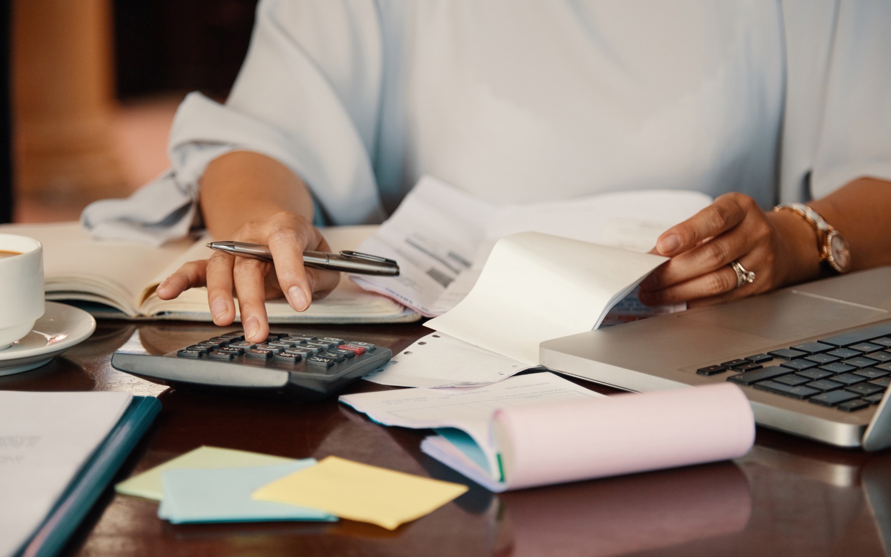 Personne utilisant une calculatrice entourée de documents et de notes pour chiffrer le budget d'un événement d'entreprise. - Article de blog Eventdrive