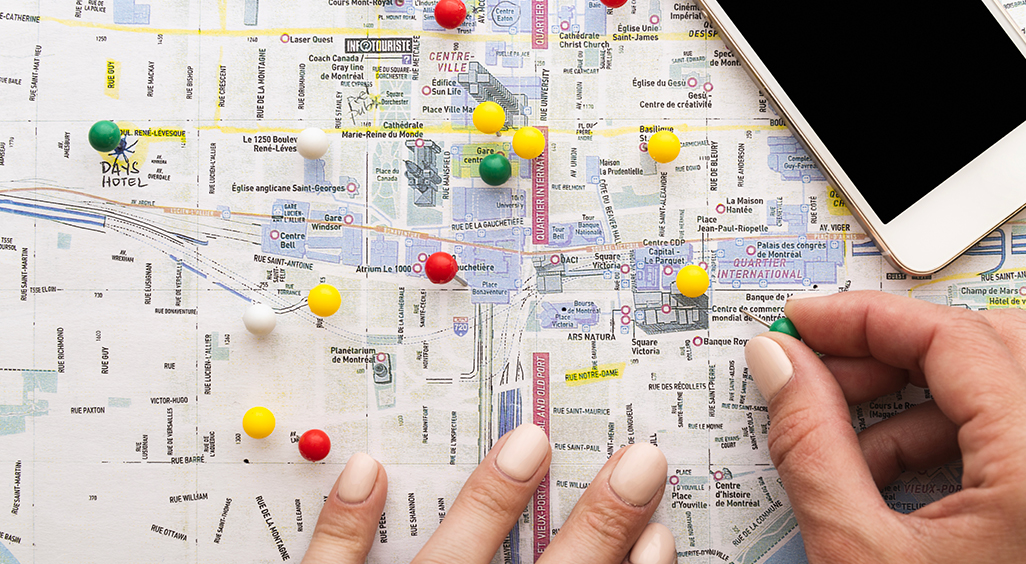 Carte de Montréal avec des punaises colorées marquant différents lieux, une main en train de placer une punaise verte, un smartphone posé en haut à droite. - Article de blog Eventdrive