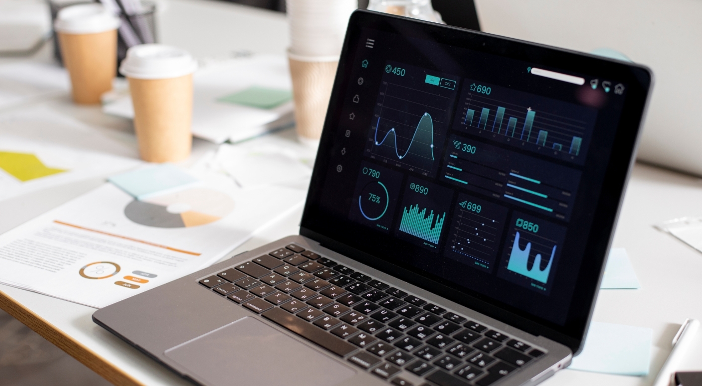 Un ordinateur ouvert sur un tableau de bord rempli de graphiques, posé sur une table avec quelques documents et des cafés autour. - Article de blog Eventdrive