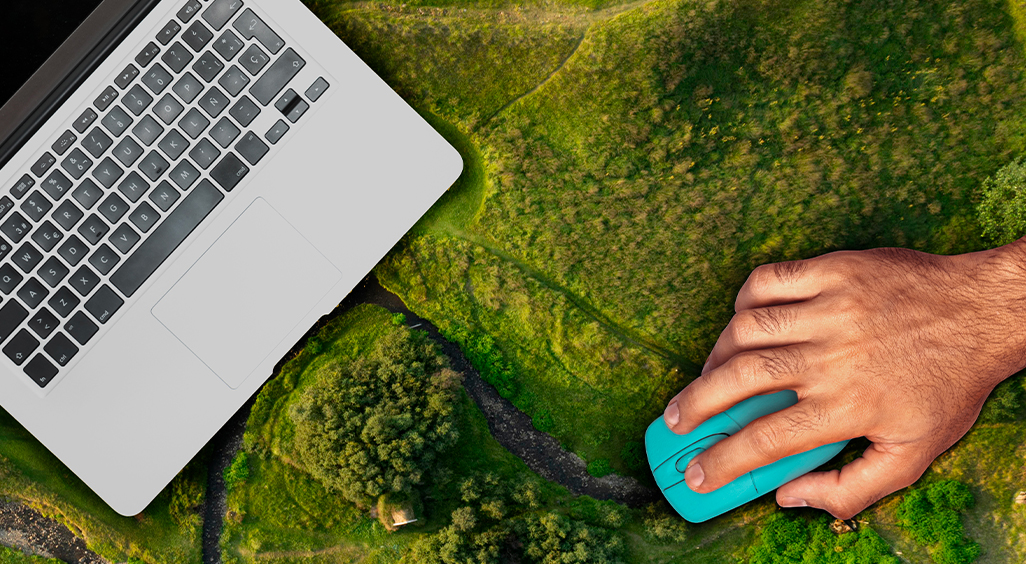 Main tenant une souris d’ordinateur sur un paysage verdoyant, à côté d’un ordinateur portable. - Article de blog Eventdrive
