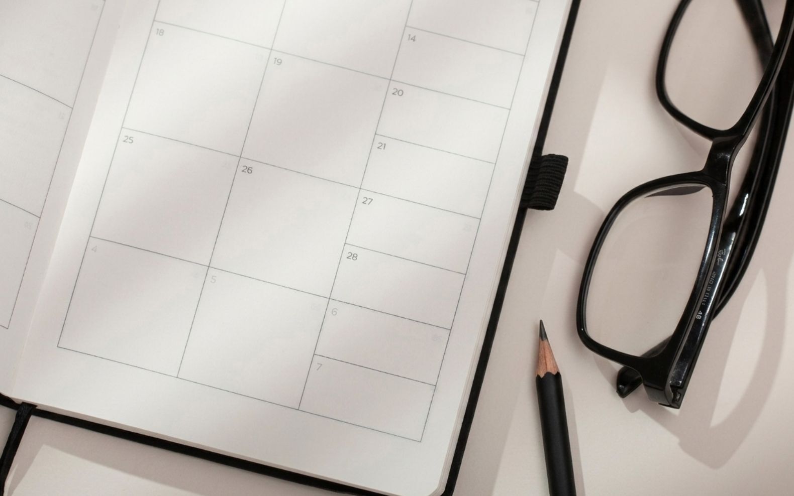 Agenda ouvert sur une page calendrier vierge, posé à côté d'un crayon et d'une paire de lunettes. - Article de blog Eventdrive