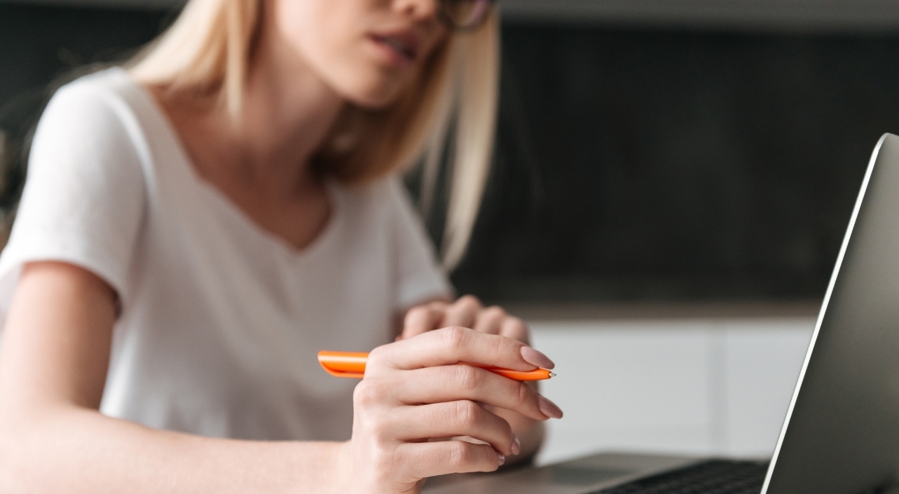 Femme travaillant sur un ordinateur portable, un stylo orange à la main, concentrée sur son écran. - Article de blog Eventdrive