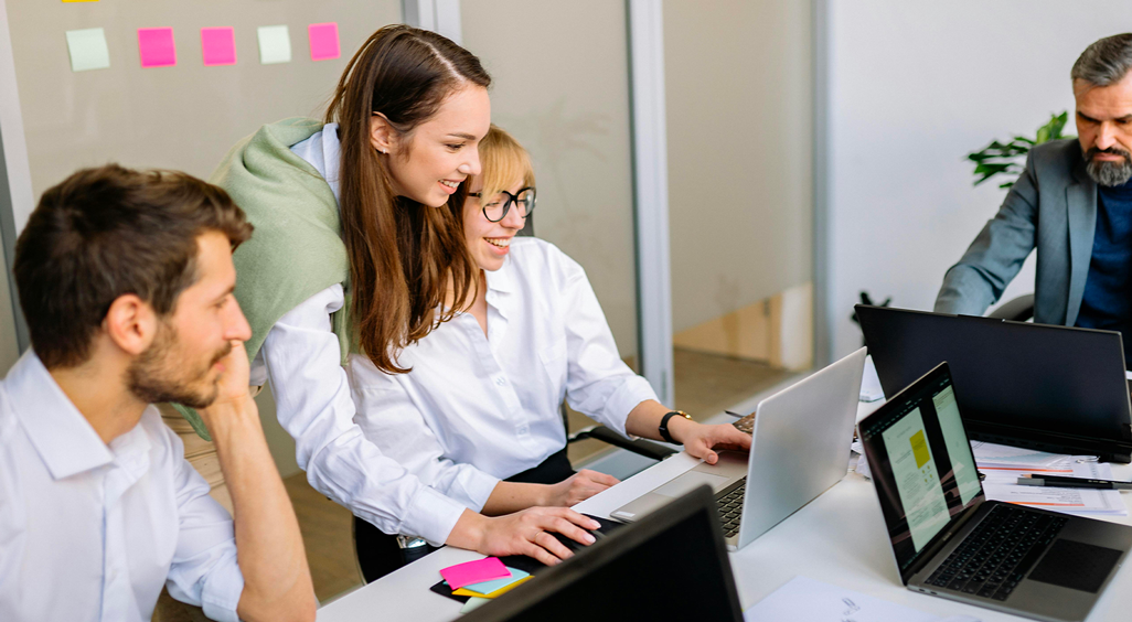 Quatre collègues en réunion, souriants, travaillant ensemble sur des ordinateurs portables dans une salle de réunion. - Article de blog Eventdrive