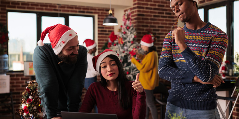 Trois personnes portant un pull et un bonnet de père Noël sont réunis devant un ordinateur.